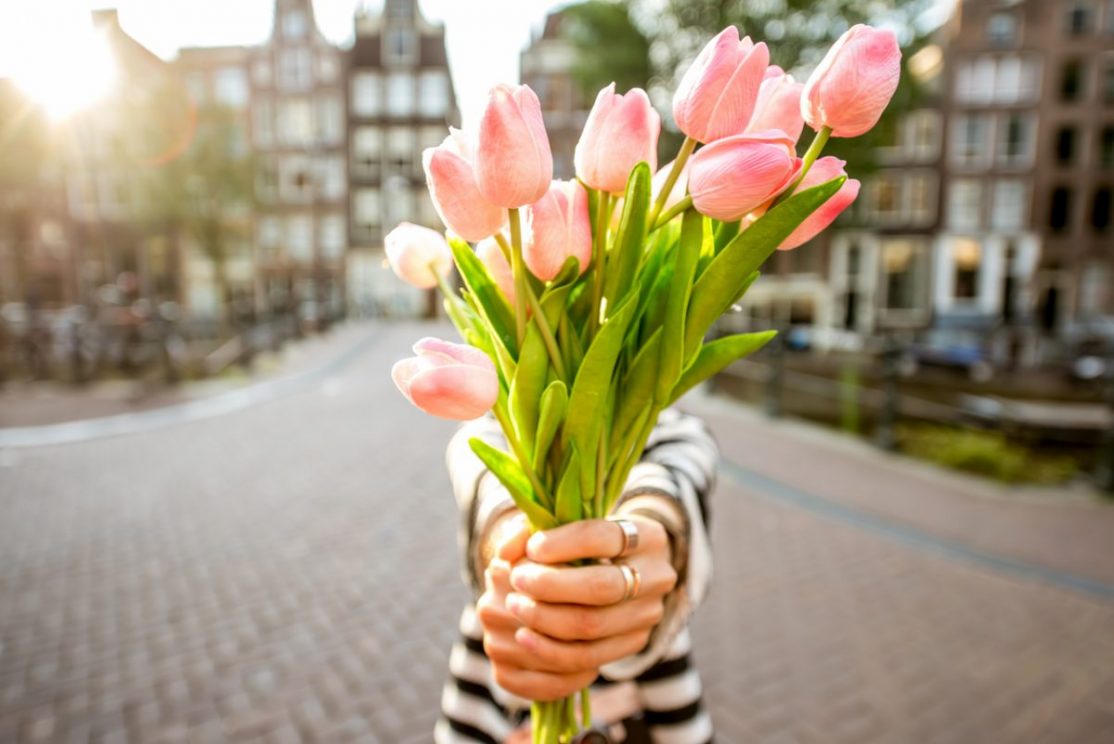 Woman giving a beautiful bouquet of pink tulips standing outdoors