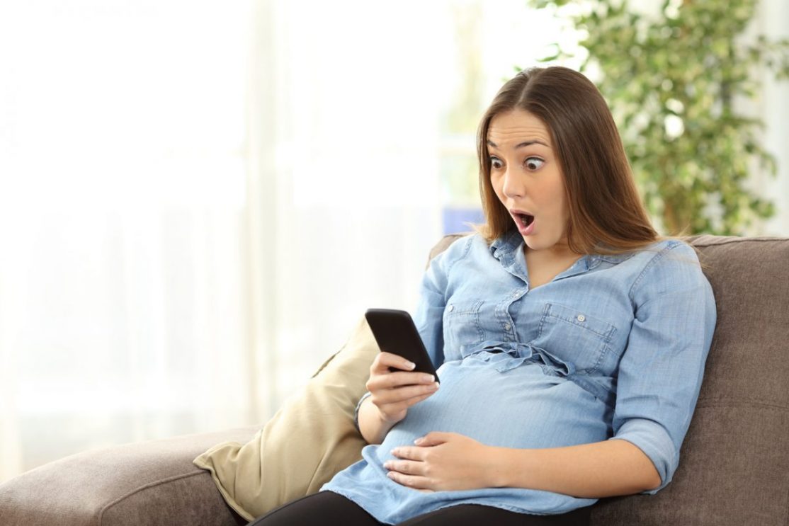 Surprised pregnant woman looking at her phone.